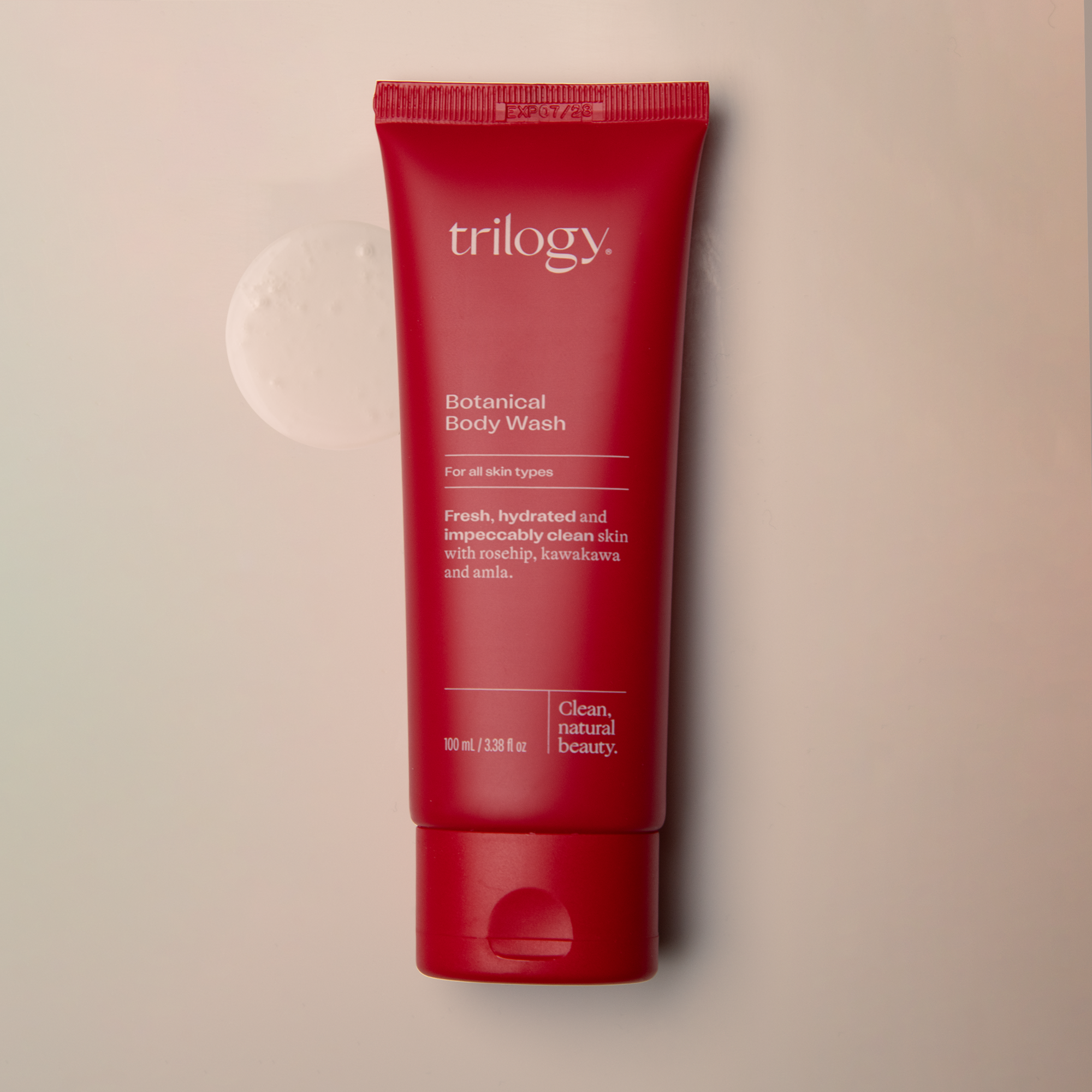 Red tube of Trilogy Botanical Body Wash on a beige background